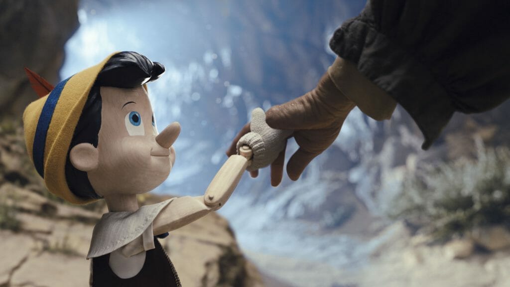 Pinocchio looks up at Geppetto with a smile while holding his hand in the 2022 live-action Disney+ remake directed by Robert Zemeckis.