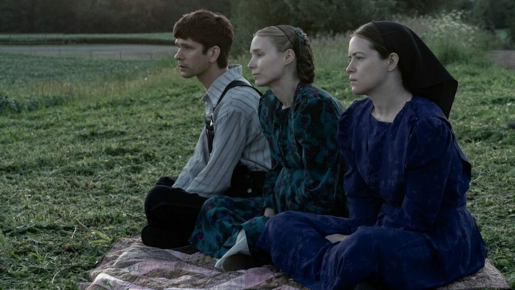 Ben Wishaw, Rooney Mara, and Claire Foy play members of an old Mennonite colony sitting together on a grassy hill in the drama film WOMEN TALKING.