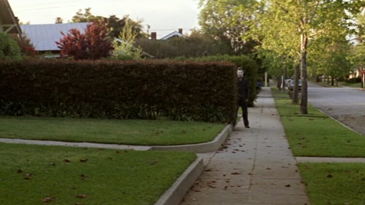The iconic shot of Michael Myers standing behind a large hedge on a front lawn from John Carpenter's original 1978 HALLOWEEN which comes in at the very top of our franchise ranked from worst to best list. 