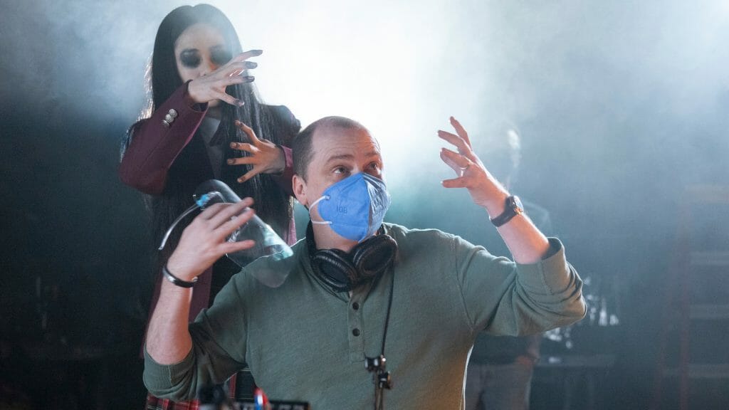 Writer and director Mike Flanagan blocks a scene on the set of the Netflix horror series THE MIDNIGHT CLUB while a young female actor in ghost makeup tries to scare him from behind.