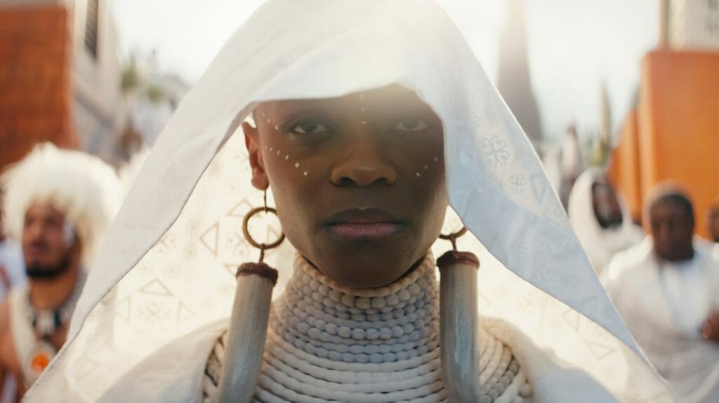 Letitia Wright as Shuri wearing her white funeral dress and large animal tooth earrings mourns her deceased brother T'Challa at his Wakandan funeral in the MCU film BLACK PANTHER: WAKANDA FOREVER.
