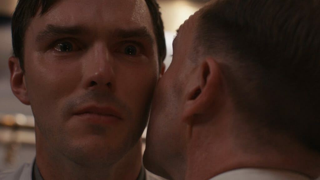 An extreme close-up shot of the obsessive and toxic foodie Tyler played by Nicholas Hoult holding in tears as Chef Slowik played by Ralph Fiennes whispers in his ear in the dark comedy horror film THE MENU. 