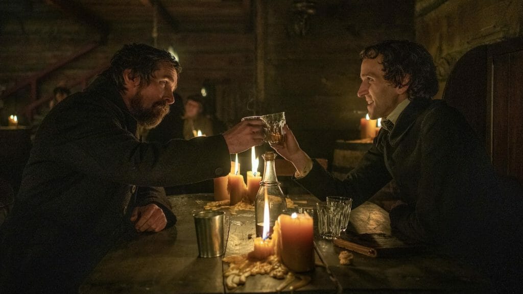 Detective Augustus Landor played by Christian Bale and the young Edgar Allen Poe played by Marry Melling share a pint at a local tavern in THE PALE BLUE EYE on Netflix.