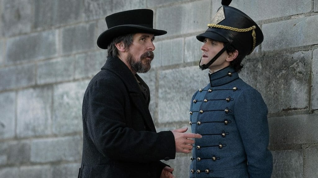 The great detective Augustus Landor played by Christian Bale confronts the young Edgar Allen Poe played by Harry Melling in his U.S. military cadet uniform in THE PALE BLUE EYE on Netflix.