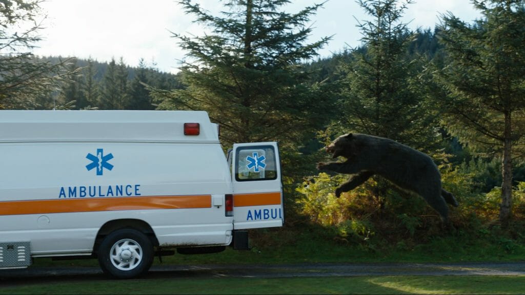 The giant 500 pound cocaine bear jumps towards an ambulance trying to escape in mid-air from the dark comedy film directed by Elizabeth Banks.