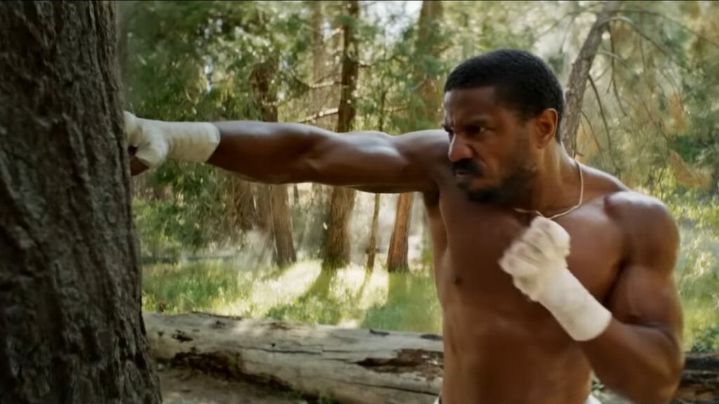 Michael B. Jordan as Adonis Creed punches a tree over and over again shirtless during the intense training montage of CREED III.
