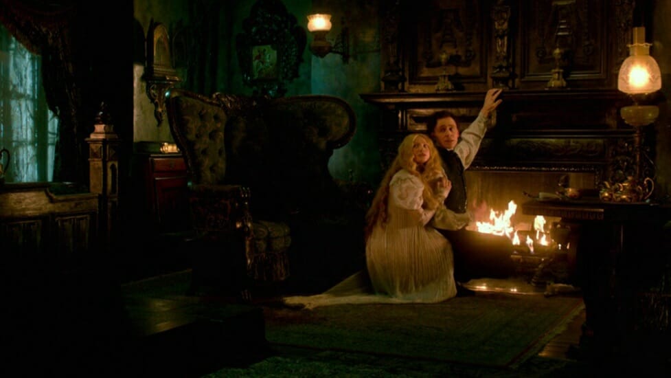 Mia Wasikowska and Tom Hiddleston hug each other by the fire place in their large haunted mansion from the Gothic Romance CRIMSON PEAK, one of our Valentine's Day films to stream for February 2023.