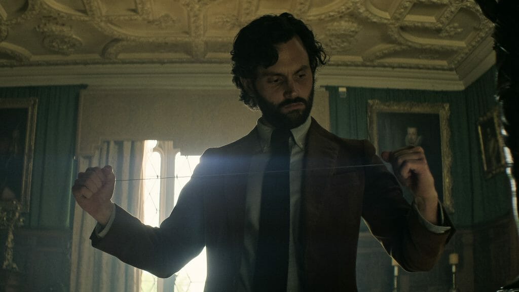 ‘You’ Season 4 Part 1 Review – A Disappointing First Half Penn Badgley as Joe Goldberg stretches out a thin piano wire in a fancy London ballroom with classic paintings on the walls in YOU Season 4 Part 1 on Netflix.