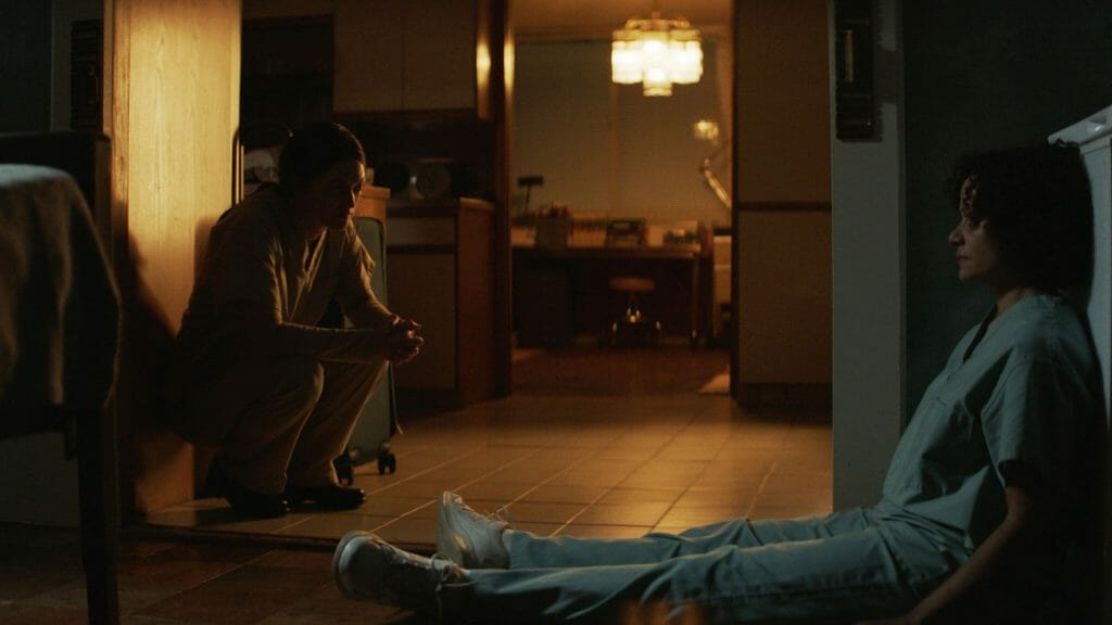 Marin Ireland as the mad scientist Dr. Rose Caspar and Judy Reyes as the desperate nurse and mother Celie sit on the floor and make plans together in the Shudder horror movie birth/rebirth. 