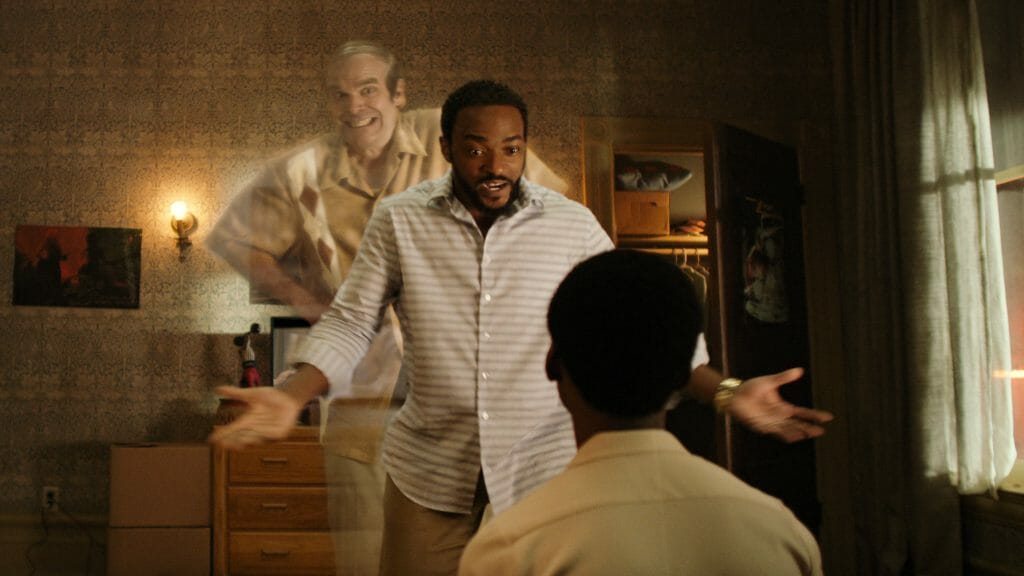 David Harbour as the friendly silent ghost Ernest makes a funny face while floating behind Anthony Mackie as he talks to his son played by Jahi Winston in the Netflix original film WE HAVE A GHOST. 