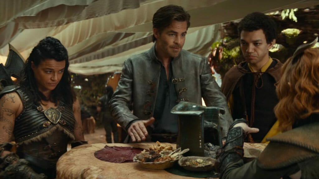 Chris Pine as the Bard Edgin Darvis devises and explains a battle plan to the barbarian warrior Holga Kilgore played by Michelle Rodriguez, the wild magic sorcerer Simon Aumar played by Justice Smith, and Doric the tiefling druid played by Sophia Lillis, who all look like they can't believe what he's saying, in the movie DUNGEONS & DRAGONS: HONOR AMONG THIEVES.