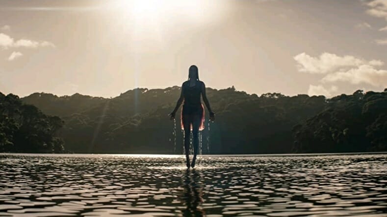 A possessed female deadite rises above the water of a huge lake in the terrifying opening title shot from the standalone horror sequel EVIL DEAD RISE directed by Lee Cronin.
