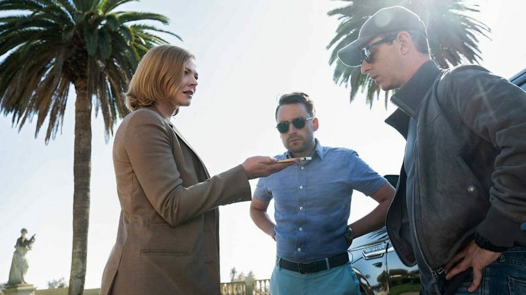 Shiv Roy played by Sarah Snook, Roman Roy played by Keiran Culkin, and Kendall Roy played by Jeremy Strong meet together in a cemetery with tall palm trees in the SUCCESSION Season 4 Premiere on HBO.