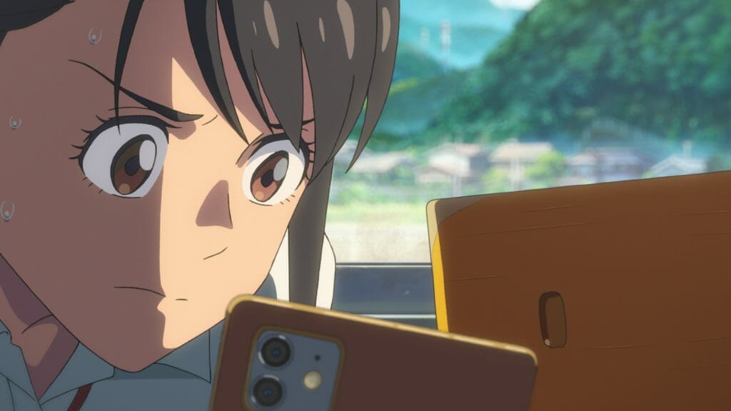 Suzume Iwato the 17-year-old student heroine voiced by Nanoka Hara stares into her phone with urgent determination in the new anime film SUZUME from writer and director by Makoto Shinkai.