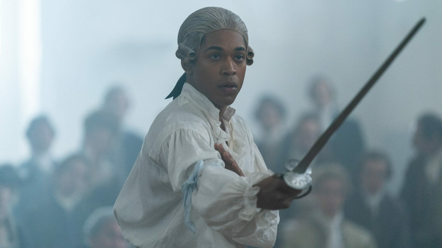Kelvin Harrison Jr. stars as the French composer Joseph Bologne, Chevalier de Saint-Georges, wearing a white wig and holding his sword in the middle of an intense fencing match in the period biopic film CHEVALIER.