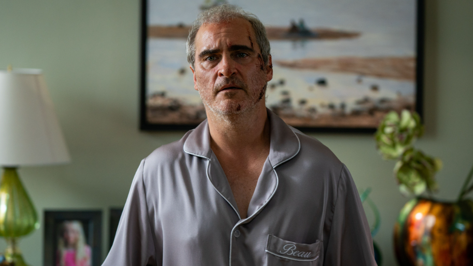 Joaquin Phoenix stars as Beau Wassermann looking defeated with bruises and scares while wearing pajamas with his named sewed on the breast pocket in the black comedy horror film BEAU IS AFRAID written and directed by Ari Aster.