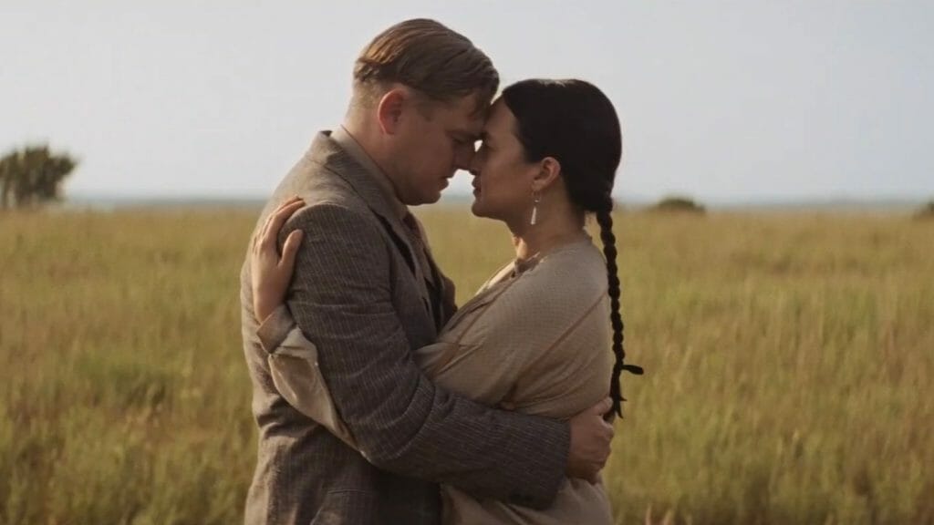Leonardo DiCaprio as Ernest Burkhart and his wife Mollie Burkhart played by Lily Gladstone hug and embrace each other in the middle of a beautiful Oklahoma field in KILLERS OF THE FLOWER MOON.