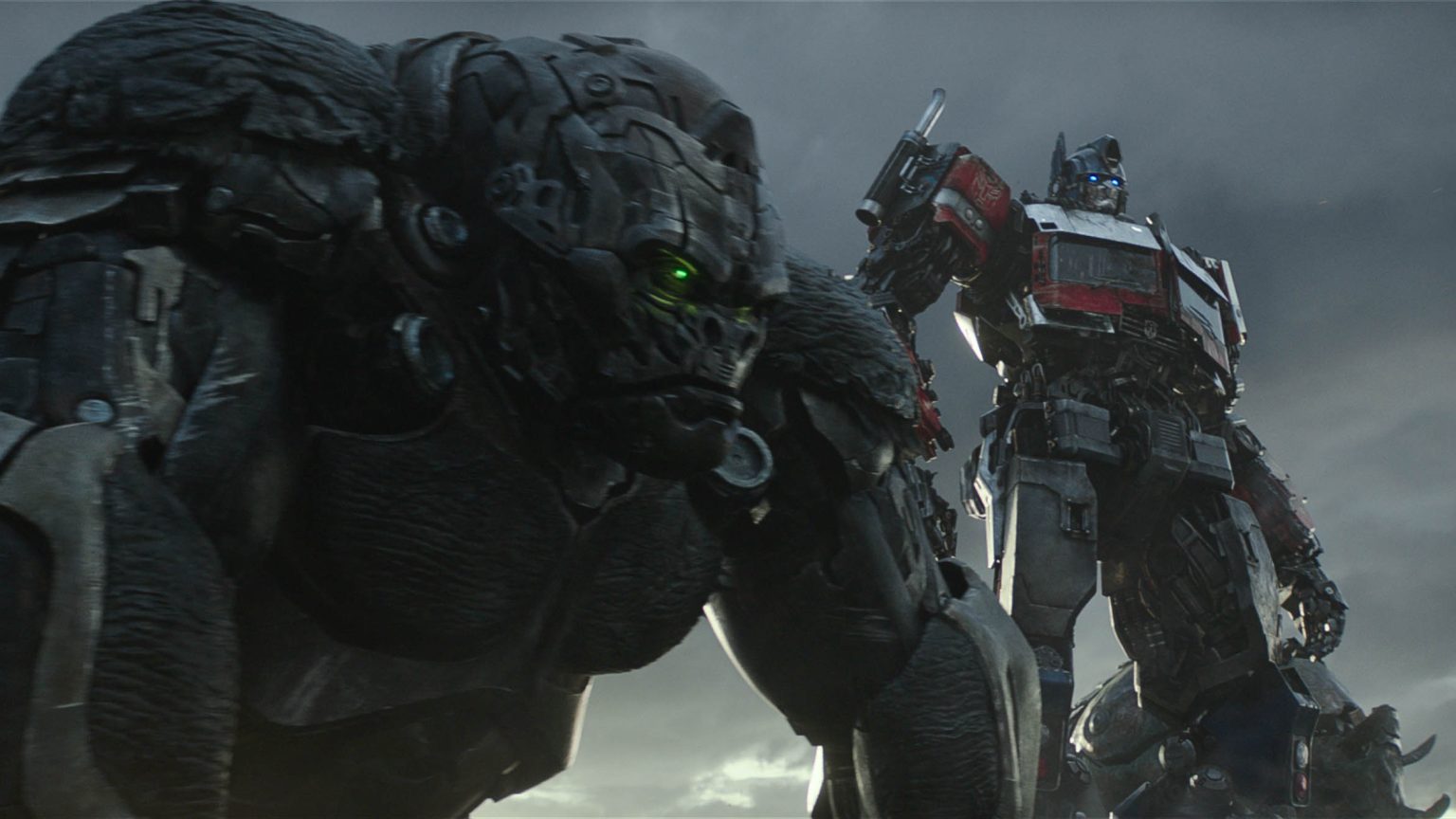 The maximal leader Optimus Primal in his huge gorilla form stands next to Optimus Prime in his classic robot form as they prepare to head into battle in TRANSFORMERS: RISE OF THE BEASTS.