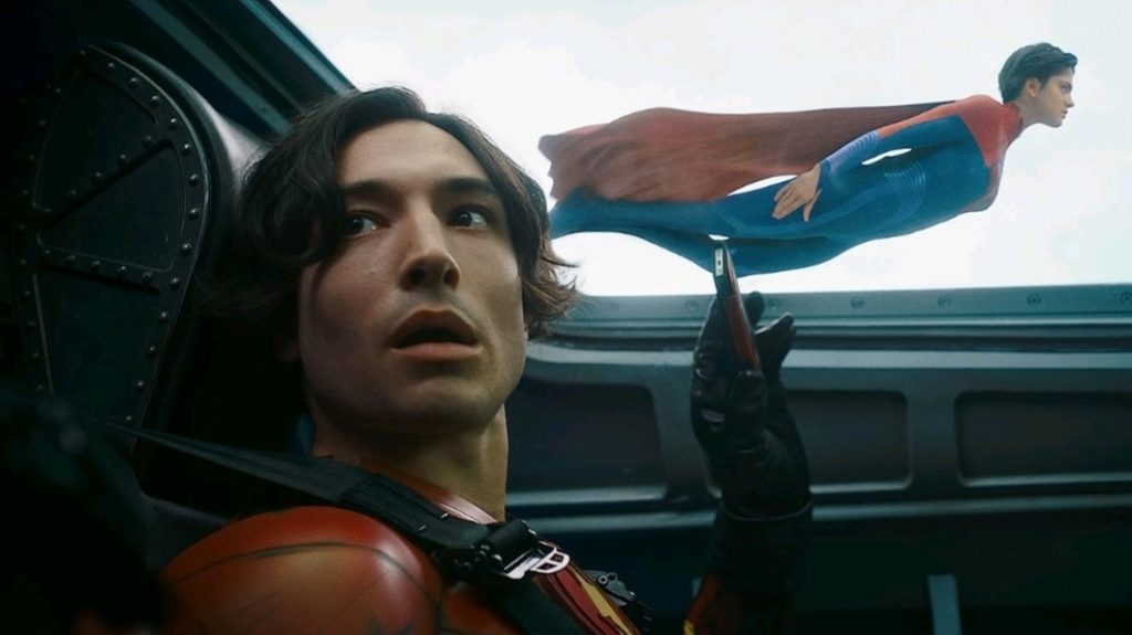 A younger version of Barry Allen played by Ezra Miller takes a photo of Supergirl played by Sasha Calle flying outisde the window of the Batwing on his phone in THE FLASH. 
