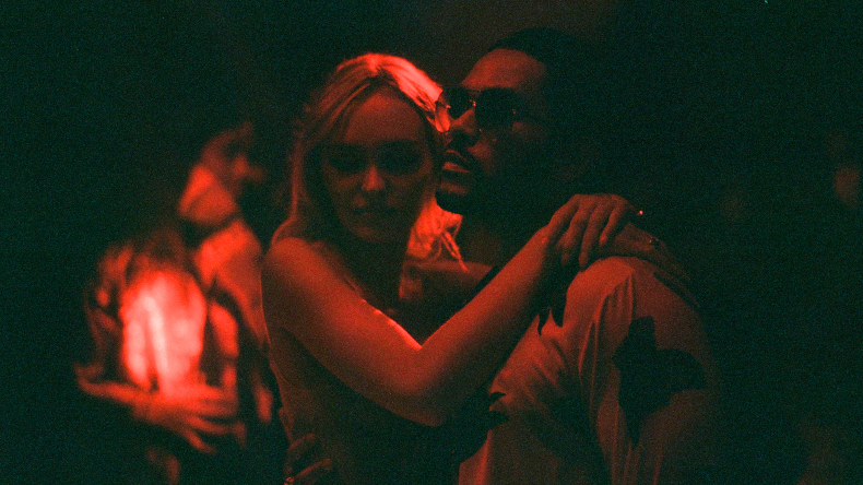 Lily-Rose Depp and Abel "The Weeknd" Tesfaye hold each other under the neon red lights of a night club in THE IDOl which is the biggest new show on HBO and Max in June 2023.
