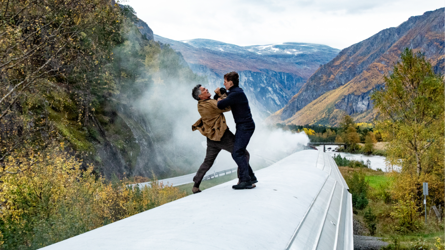 Ethan Hunt and the main villain Gabriel fight each other with knives on top of a train moving fast through a beautiful valley with huge mountains in the background in MISSION: IMPOSSIBLE - DEAD RECKONING PART ONE.  
