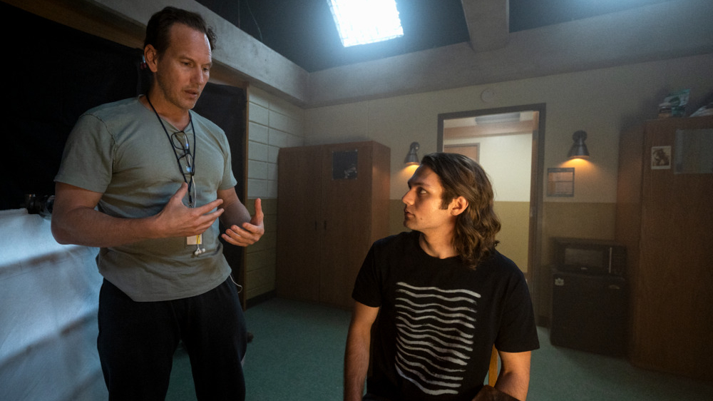 Director Patrick Wilson gives notes to actor Ty Simpkins on a college dorm room set from the behind the scenes of INSIDIOUS: THE RED DOOR. 