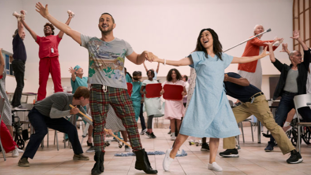 Frenchie and Kimiko hold hands and sing together in the middle of large colorful musical number with background dancers in THE BOYS Season 3. 