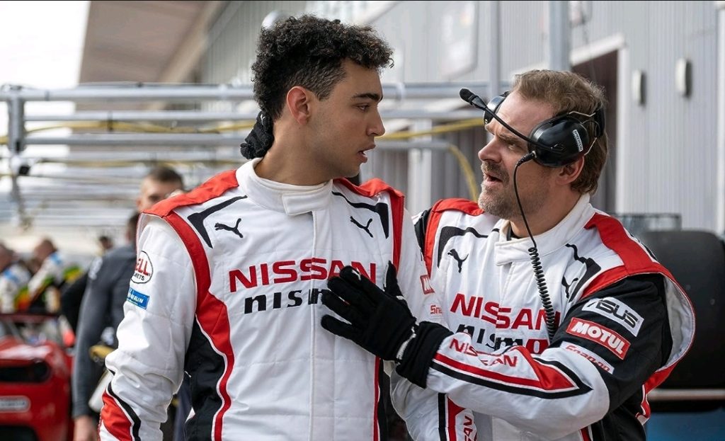 Archie Madekwe and David Harbour both wear Nissan gear on the race track as Harbour gives him some advice as his coach in the GRAN TURISMO movie.