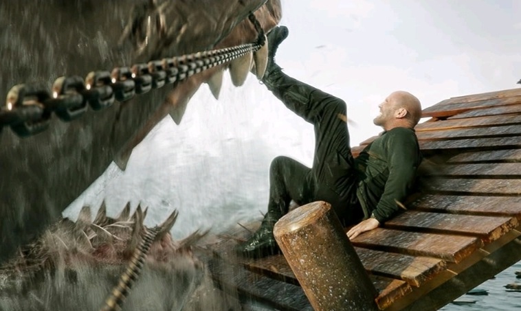 Jason Statham pushes himself back from the open jaws of a colossal Megalodon trying to eat him on a broken pier in MEG 2: THE TRENCH.