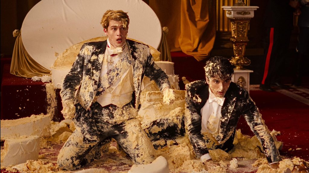 Nicholas Galitzine and Taylor Zakhar Perez fall on the ground covered in cake all over their fancy attire in RED, WHITE & ROYAL BLUE on Amazon Prime Video.