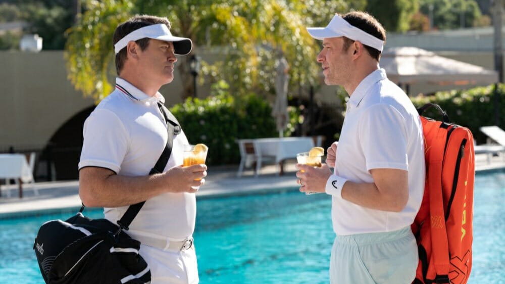 Nick Offerman stars as Kenneth C. Griffin and Seth Rogan stars as Gabe Plotkin talking together in their Tennis clothes by a fancy pool in the movie DUMB MONEY.