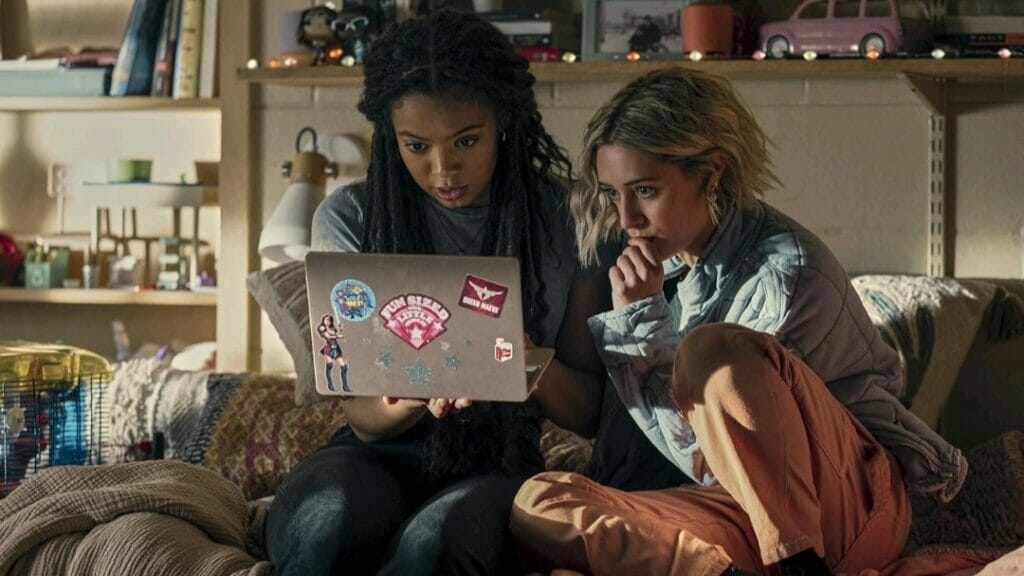 Jaz Sinclair and Lizze Broadway sit together in a college dorm and eagerly watch a video on a laptop with superhero stickers on it in The Boys spin-off series GEN V on Prime Video.