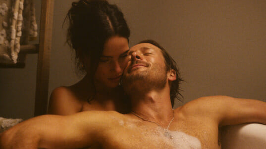 Adria Arjona and Glen Powell take a romantic bath together with bubbles in the action romantic comedy movie HIT MAN. 