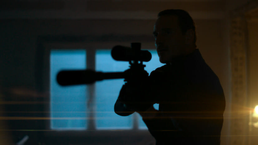 A dark silhouette of Michael Fassbender aiming a sniper rifle in the Netflix movie THE KILLER directed by David Fincher.