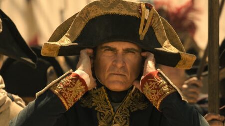 Napoleon Bonaparte played by Joaquin Phoenix wears his giant military hat and covers his ears as he waits for cannons to go off in the middle of a huge battle from the historical epic NAPOLEON directed by Ridley Scott.