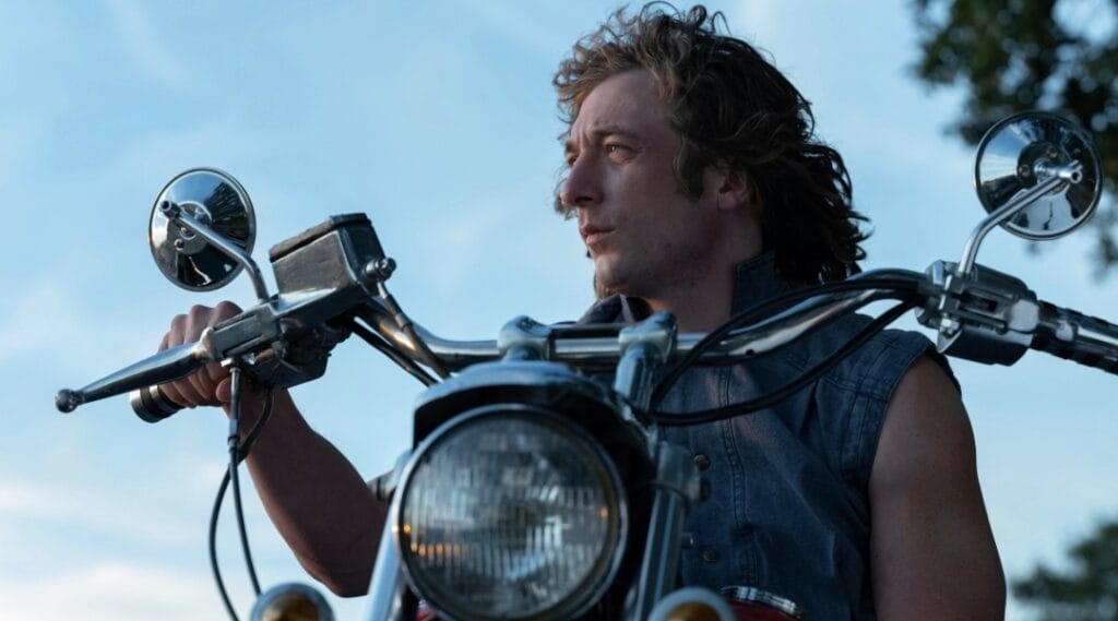 Jeremy Allen White stars as famous wrestler Kerry Von Erich posing on his motorcycle in a cool denim vest in the A24 movie THE IRON CLAW.