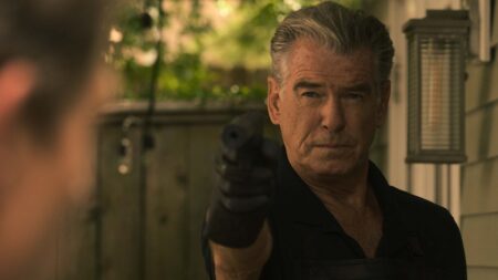 Pierce Brosnan stars as aging hitman and fixer Charlie Swift pointing a gun with a silencer with his black latex gloves on as he gets ready to take out his next target in the movie FAST CHARLIE.