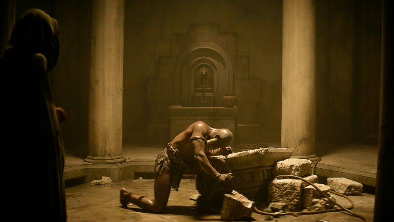 Djimon Hounsou stars as General Titus kneeling in the middle of an ancient bath showing off his muscles shirtless in REBEL MOON - PART ONE: A CHILD OF FIRE on Netflix.