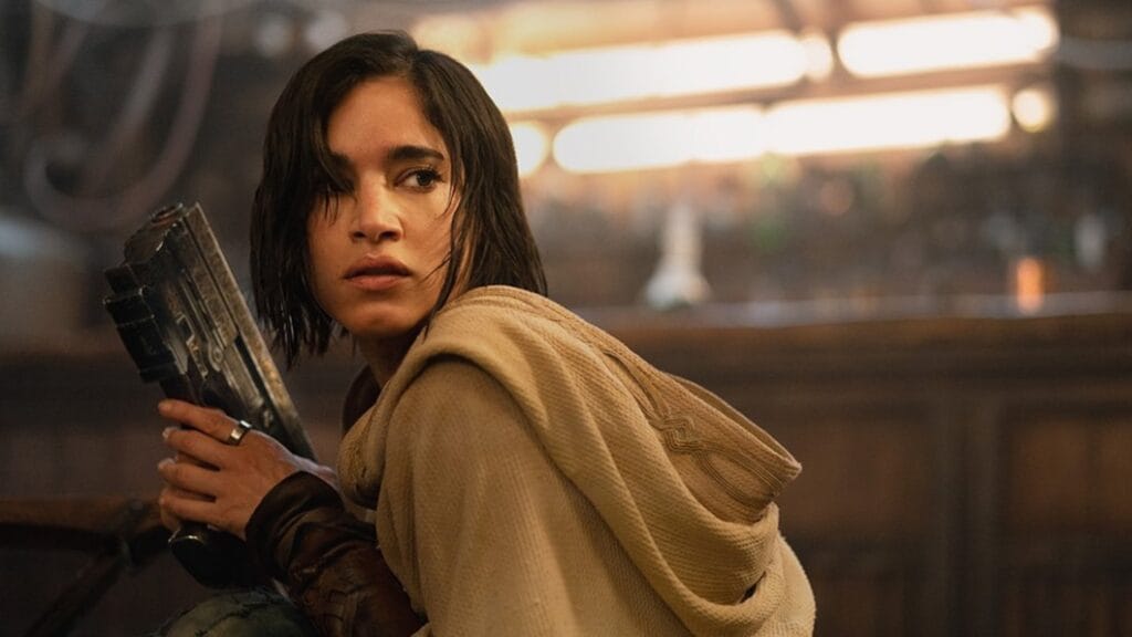 Sofia Boutella stars as the Rebel warrior Kora posing with her signature regal laser gun in REBEL MOON - PART ONE: A CHILD OF FIRE on Netflix.