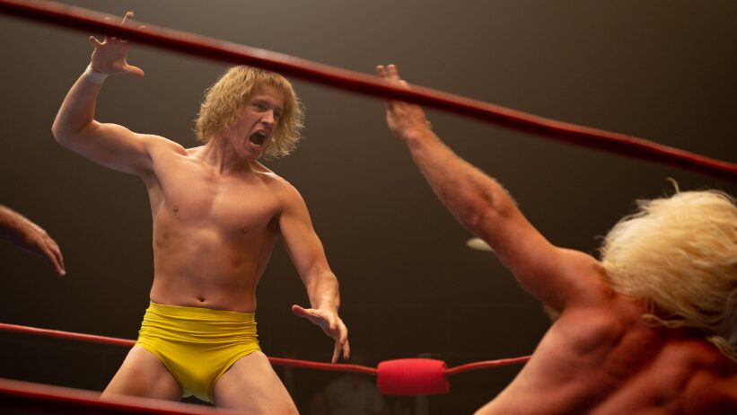 Harris Dickinson stars as David Von Erich yelling fiercely and raising his hand before giving the iconic Iron Claw move to his opponent falling on the floor in the wrestling ring in THE IRON CLAW film.