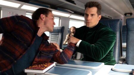 Henry Cavill stars as Agent Argylle wearing his signature green velvet suit and holding a goon's fists down while sitting in a train cart looking as if he's not even struggling to put up a fight in the spy action comedy film ARGYLLE.