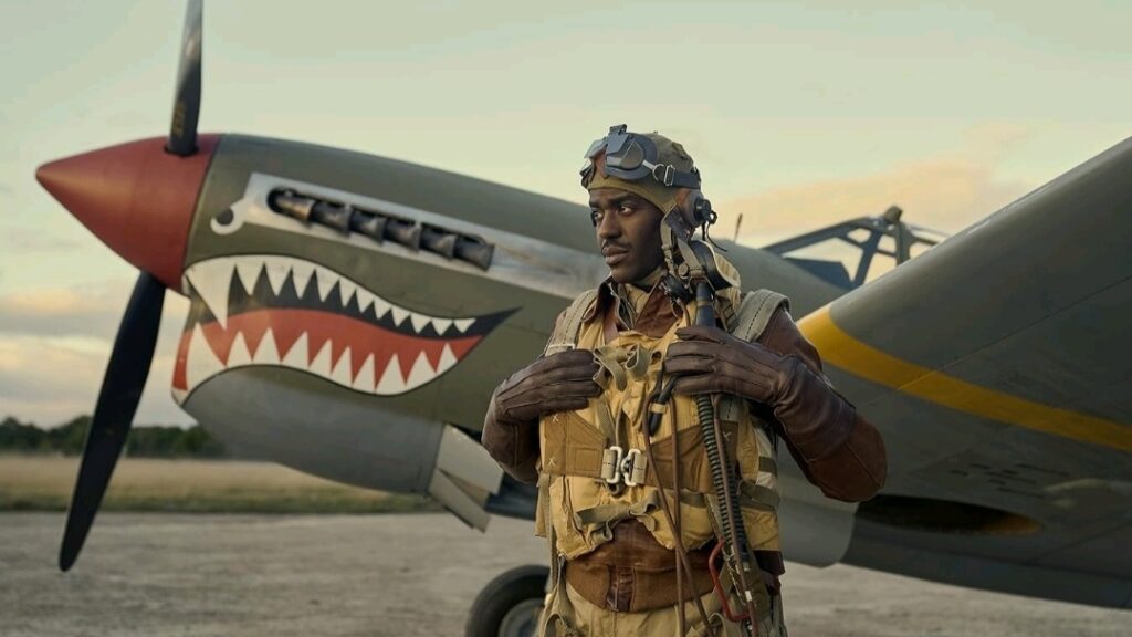 Ncuti Gatwa stars as 2nd Lt. Robert H. Daniels of the Tuskegee Airmen posing in full gear in front of his fighter plane with a shark's eyes and sharp teeth painted on the nose in the MASTERS OF THE AIR miniseries.