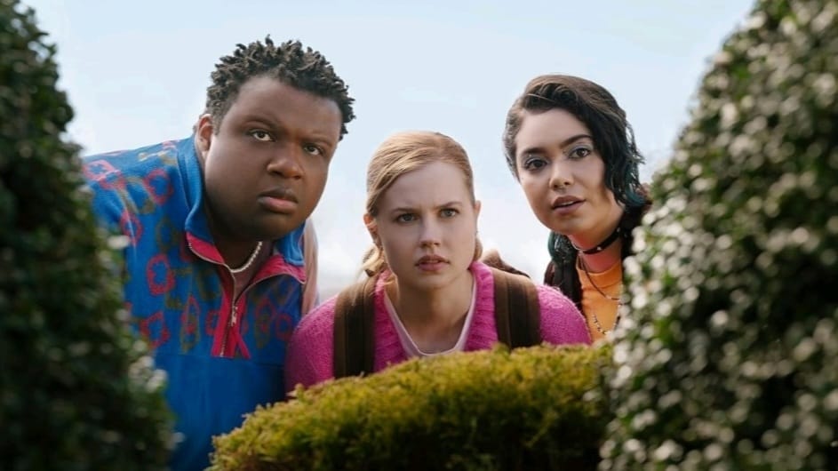 Jaquel Spivey, Angourie Rice, and Auliʻi Cravalho star as Damian, Cady, and Janis hiding behind a hedge at school in the 2024 movie musical version of MEAN GIRLS.