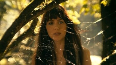 Dakota Johnson stars as Cassie Web staring into a large spider web between some trees in the middle of the Amazon rain forest in the Marvel superhero film MADAME WEB.