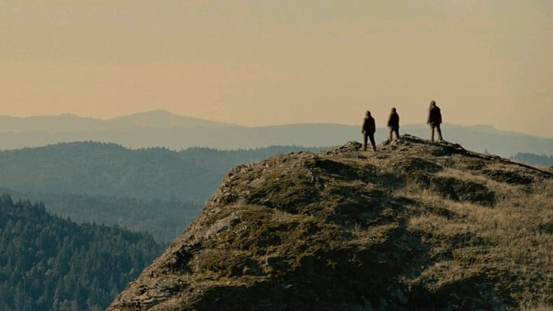 Jesse Eisenberg, Riley Keough, and Christophe Zajac-Denek star as a family of three Bigfoots in full costume overlooking a vast valley on top of a beautiful mountain in the movie SASQUATCH SUNSET.