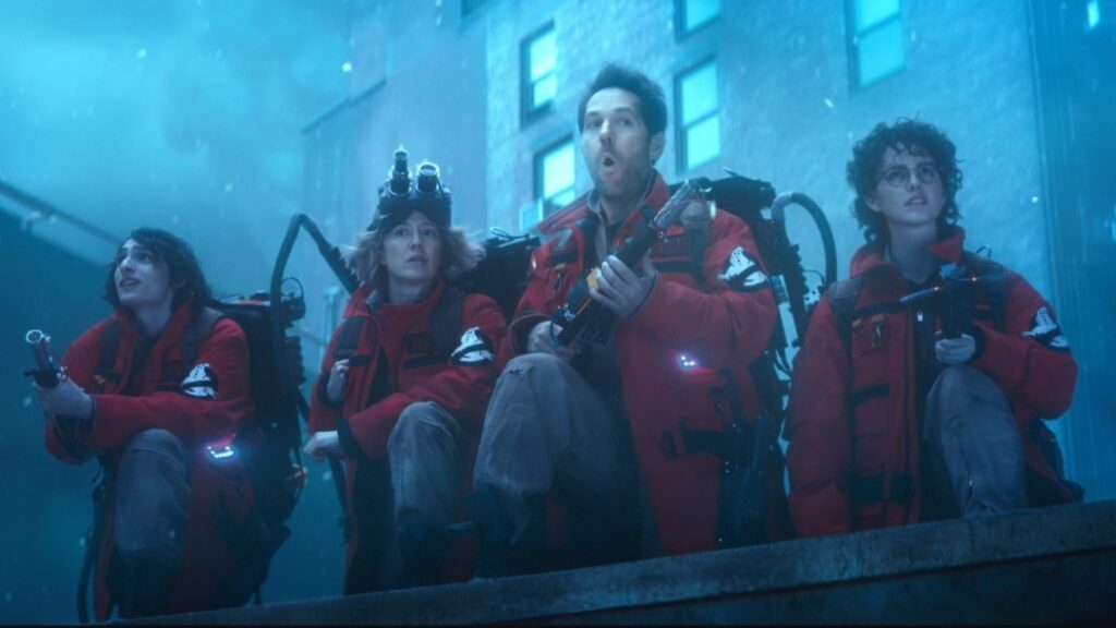 Finn Wolfhard, Carrie Coon, Finn Wolfhard, and McKenna Grace pose together in their new red Ghostbuster suits and proton packs in the legacy sequel GHOSTBUSTERS: FROZEN EMPIRE.