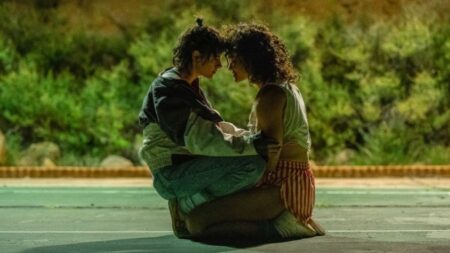 Lou played by Kristen Stewart and Jackie played by Katy O'Brian embarce each other with a huge as they sit in the middle of an empty lot in the A24 romantic thriller film LOVE LIES BLEEDING.