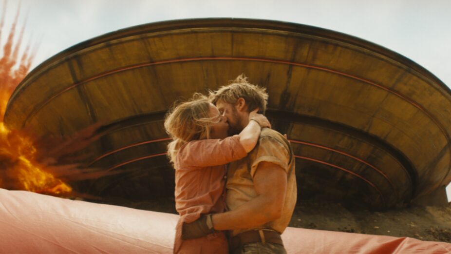 Ryan Gosling and Emily Blunt embrace each other with a huge and a romantic kiss in front of an exploding giant saucer on the set of a movie in the action rom-com THE FALL GUY. 