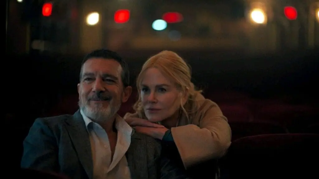 Nicole Kidman leans over Antonio Banderas' shoulder as he directs dress rehearsals in a large empty theater from the first few rows in the erotic thriller film BABYGIRL. 