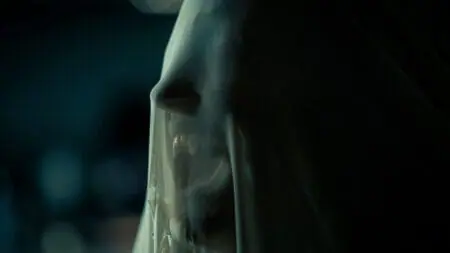 A vampire shows off its teeth while under a white cloak in the 2024 film adaptation of Stephen King's SALEM'S LOT.